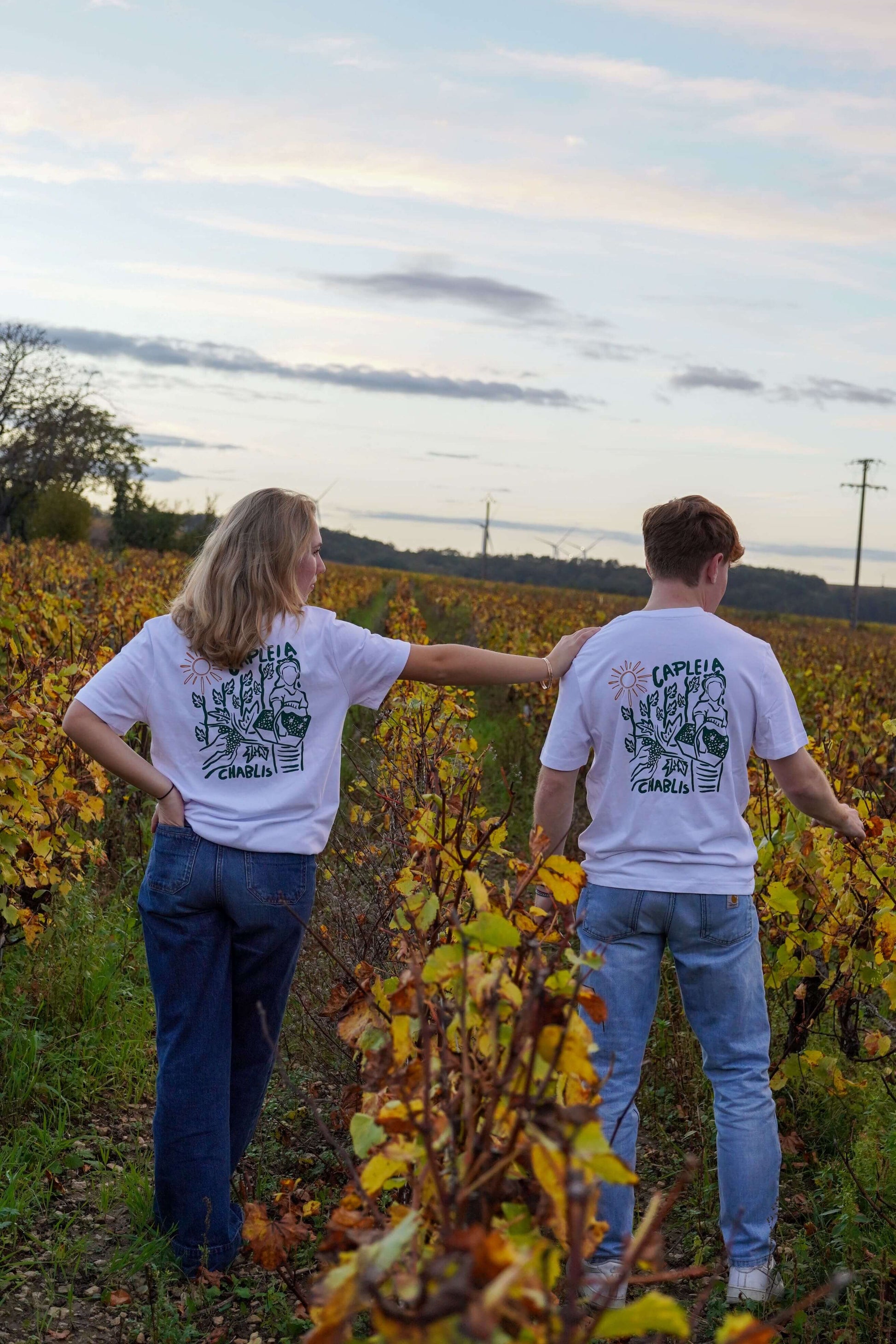 Couple wearing organic cotton t-shirts in vineyard during harvest, showcasing relaxed fit and nature-themed design.