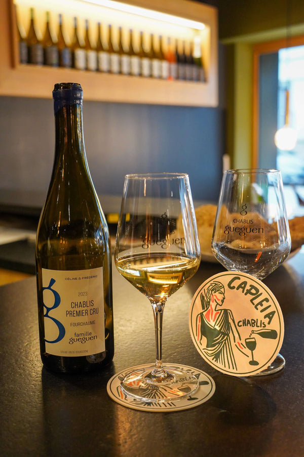 Bouteille de Chablis Premier Cru avec verre et dessous de verre artistique, illustrant un moment convivial autour du vin.