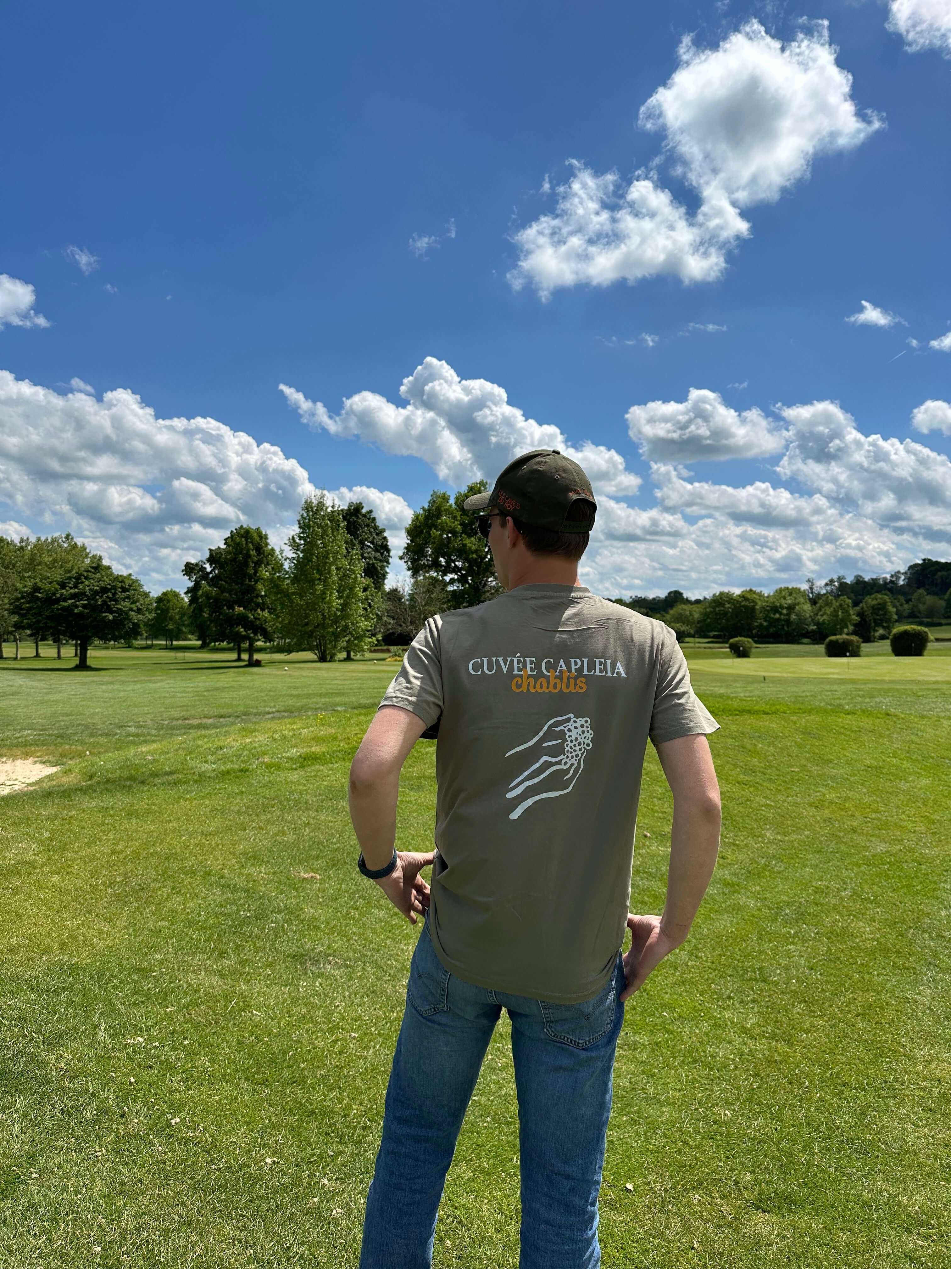 Image of Homme portant un t-shirt Cuvée Capleia en coton biologique, coupe décontractée, sur un terrain de golf.