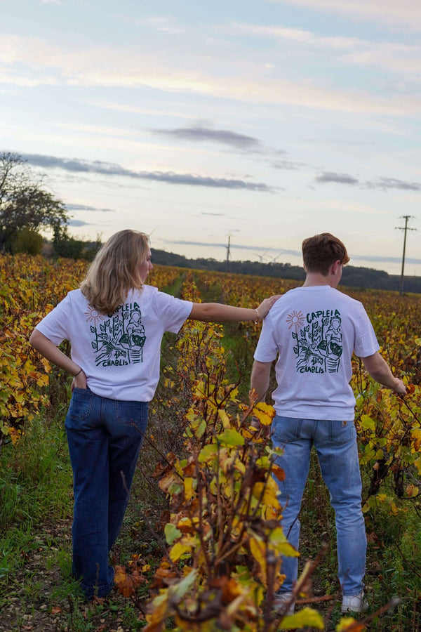 Couple wearing organic cotton t-shirts in vineyard during harvest, showcasing relaxed fit and nature-themed design.