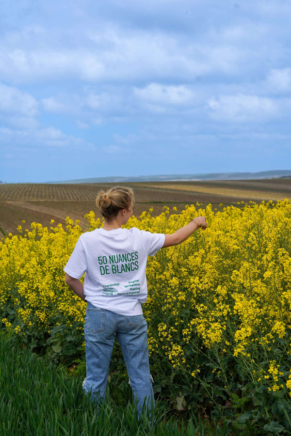 Person wearing '50 Nuances de Blancs' t-shirt in a field of yellow flowers, showcasing casual style.
